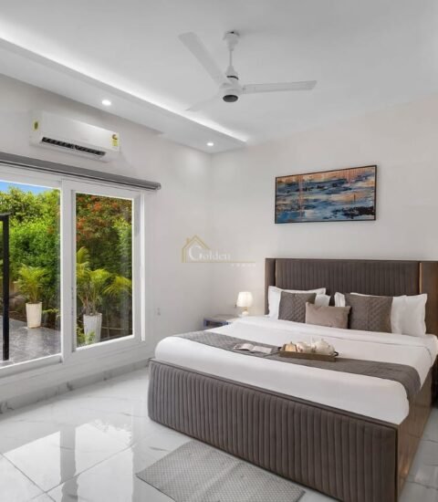 Farmhouse bedroom with a wall-mounted AC, grey bed, two table lamps and a window opening to the garden