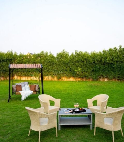 Garden swing with cushions and four wicker chairs on a green lawn with a hedge and cabana behind