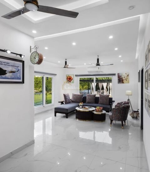Bright farmhouse living room with a grey sofa, round coffee tables, ceiling fans and framed art along the hallway