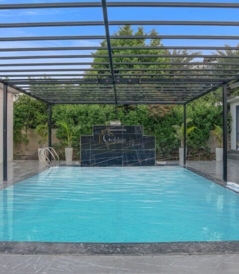 Pool deck with two wicker chairs, a round side table and a black marble feature wall beside the pool