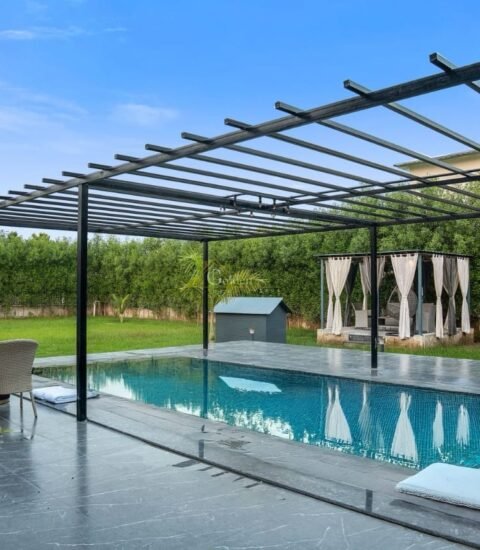 Clear blue pool with a steel ladder beside the white farmhouse, with reflections on the water